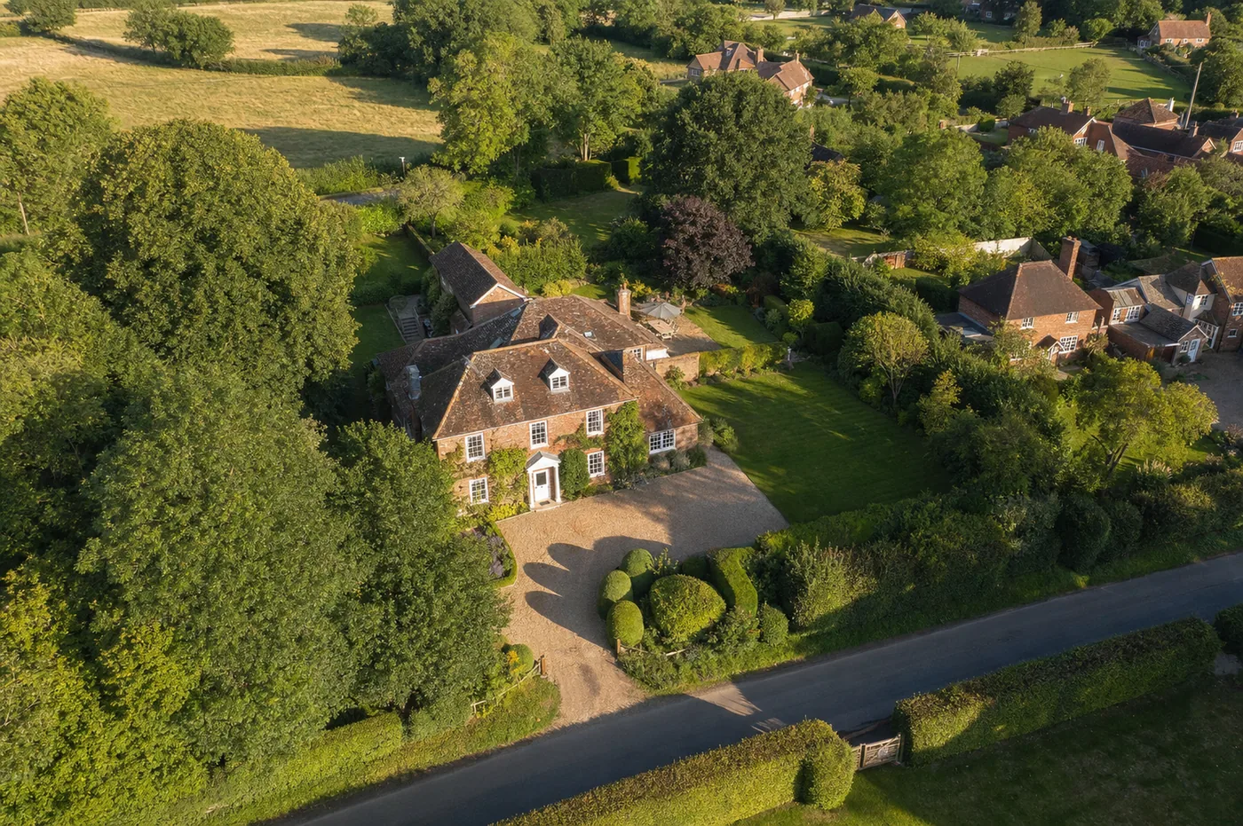 Aerial view of a detached brick house with large garden, gravel drive and mature trees